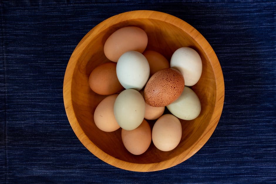 Colorful chicken eggs in shades of brown, blue, and green in a wooden bowl